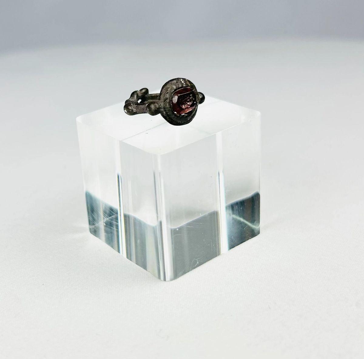 Ancient silver ring from the Eastern Mediterranean or Near East, Late Roman to Early Byzantine period (circa 300–600 CE), featuring a deep red garnet intaglio engraved with symbolic imagery, flanked by decorative silver nodes, preserving its historical elegance and craftsmanship.