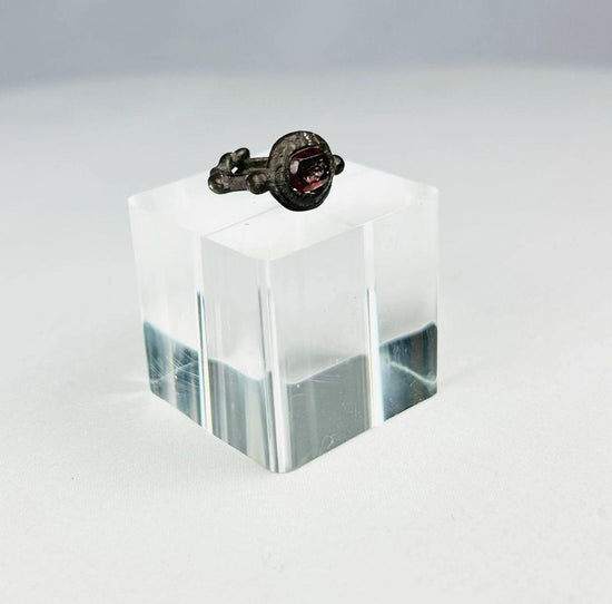 Ancient silver ring from the Eastern Mediterranean or Near East, Late Roman to Early Byzantine period (circa 300–600 CE), featuring a deep red garnet intaglio engraved with symbolic imagery, flanked by decorative silver nodes, preserving its historical elegance and craftsmanship.