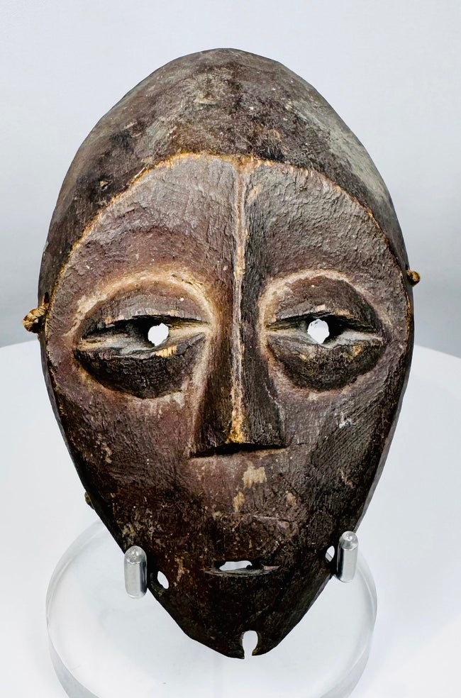Central African Lega mask featuring simplified symbolic facial features and original fiber cord remnants.
