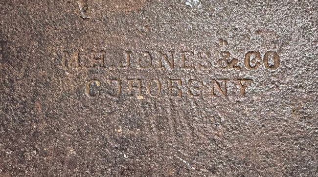 Close-up of the M.H. Jones &amp; Co. maker’s mark stamped into the forged steel of the 19th-century axe head.