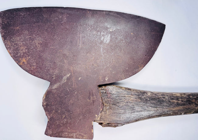 Close-up of an antique American broad axe head showing its wide curved cutting blade and aged forged steel surface.
