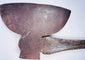 Close-up of an antique American broad axe head showing its wide curved cutting blade and aged forged steel surface.