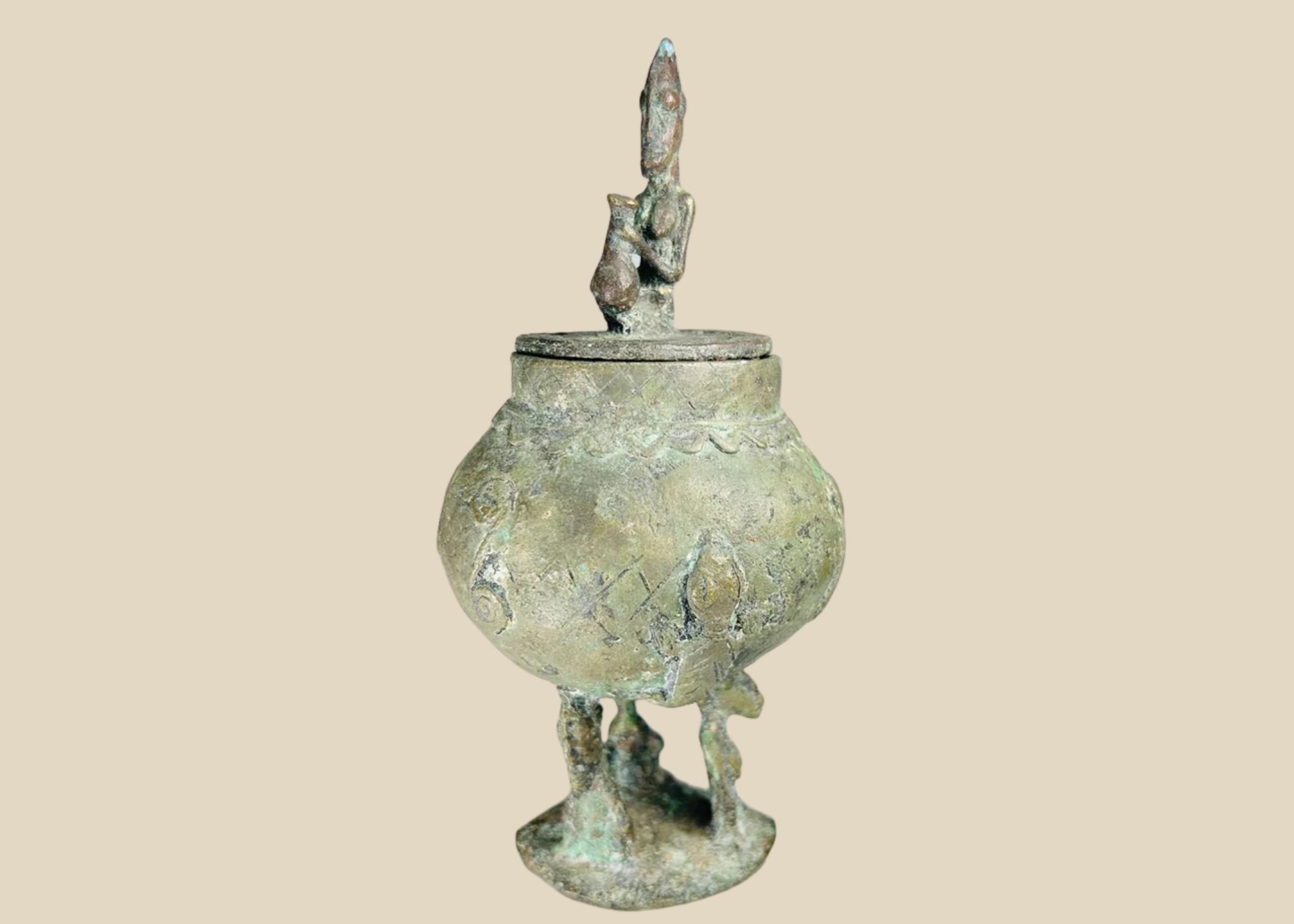 19th-century Dogon bronze container from Mali with bulbous body, engraved motifs, anthropomorphic legs, and a sculpted human figure on the lid, used in ritual and healing practices.