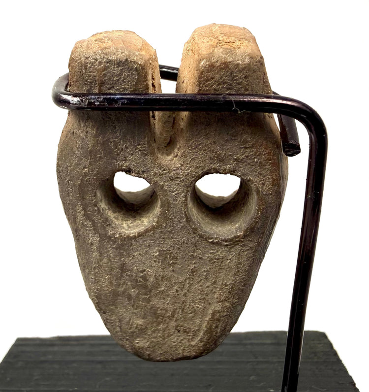 Stylized human face carving with symmetrical round eye holes and central nose bridge