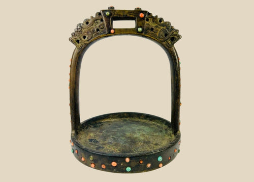 Ornate cast bronze stirrup from Mongolia or Himalayan region, featuring dragon-head terminals, pierced latticework, and hand-set coral, turquoise, and glass inlays, 7 inches tall by 6 inches wide, with natural patina and verdigris, circa 18th century.