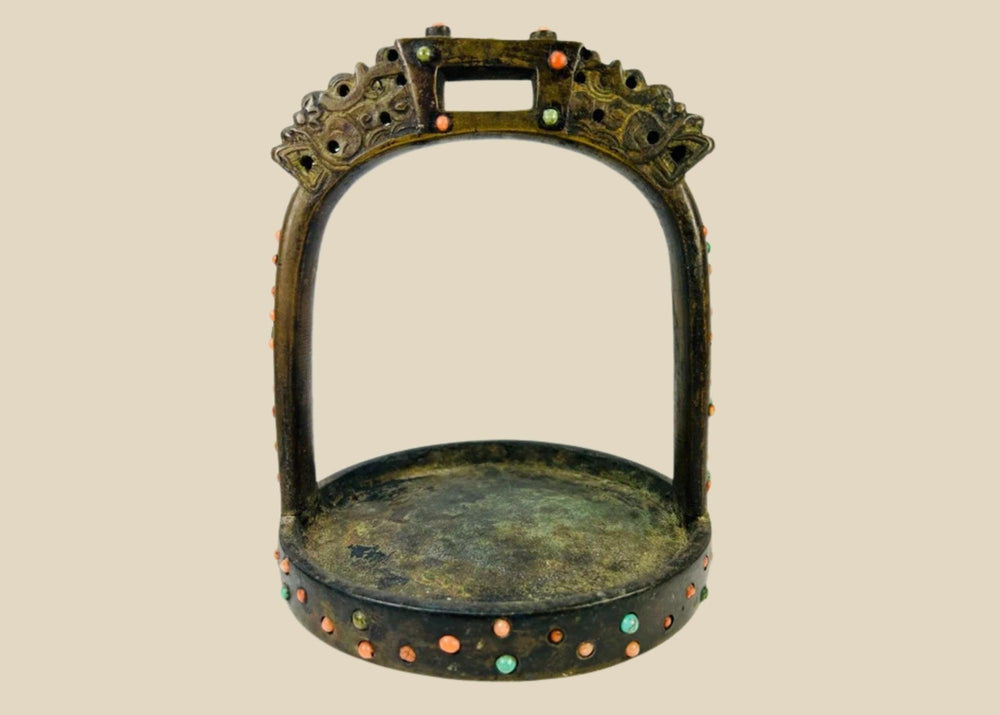 Ornate cast bronze stirrup from Mongolia or Himalayan region, featuring dragon-head terminals, pierced latticework, and hand-set coral, turquoise, and glass inlays, 7 inches tall by 6 inches wide, with natural patina and verdigris, circa 18th century.