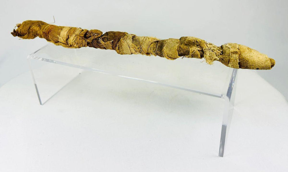 Mummified juvenile crocodile from Ancient Egypt, Late Period to Early Roman era, wrapped in linen as a votive offering to the god Sobek, displayed on a clear stand.