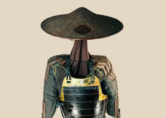 Authentic Japanese samurai armor from the Muromachi Period (1333–1573), featuring black-lacquered cuirass with gold accents, kote sleeves with chainmail reinforcement, dark-blue silk lacing, and a lacquered jingasa war hat bearing the Takeda clan crest, displayed on a wooden stand against a white background
