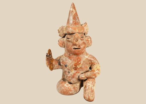 Hollow West Mexican Nayarit seated terracotta figure with tall conical headdress, turban band, large earspools, and raised right hand holding an attribute, featuring red and cream slip remnants, mineral accretions, and mounted on a modern wood display block, ca. 100 BCE–300 CE