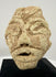 Ancient Mesopotamian-style stone sculpture featuring deeply incised eyes, geometric facial details, and a weathered surface.