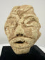 Ancient Mesopotamian-style stone sculpture featuring deeply incised eyes, geometric facial details, and a weathered surface.