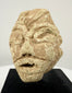 Carved limestone head fragment inspired by ancient Near Eastern votive traditions, mounted on a modern black display stand.