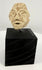 Ancient Mesopotamian-style carved stone head fragment featuring almond-shaped eyes, a broad nose, and a simplified mouth.