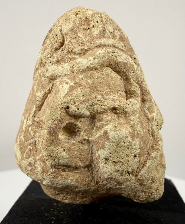 Frontal close-up of carved limestone face with abstract geometric features and heavy brows