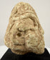 Frontal close-up of carved limestone face with abstract geometric features and heavy brows