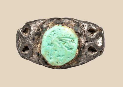 Ancient Neo-Assyrian silver ring from Mesopotamia (modern-day Iraq), 9th–7th century BCE, featuring a raised turquoise bezel and engraved winged serpent with mythical beast motifs. Silver band with natural patina showcases Assyrian craftsmanship, symbolizing divine protection, authority, and spiritual power.