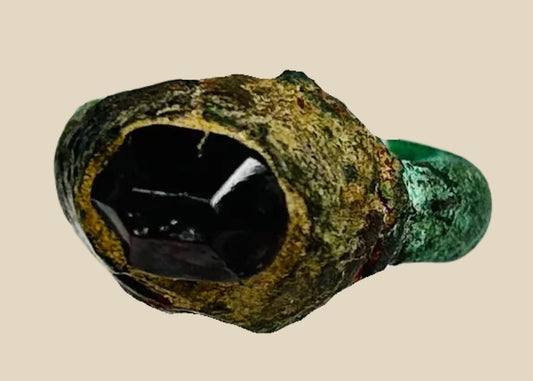 An ancient Neo-Assyrian bronze ring with a deep red garnet intaglio in a raised bezel, natural green patina on the band, dating to the 9th–7th century BCE.