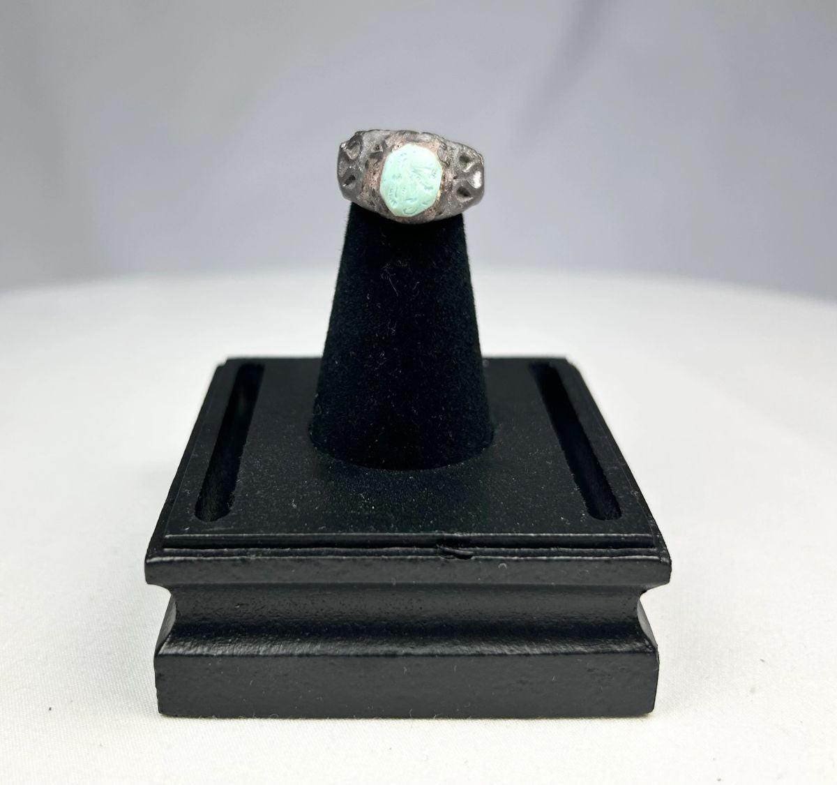 Ancient Neo-Assyrian silver ring from Mesopotamia (modern-day Iraq), 9th–7th century BCE, featuring a raised turquoise bezel and engraved winged serpent with mythical beast motifs. Silver band with natural patina showcases Assyrian craftsmanship, symbolizing divine protection, authority, and spiritual power.