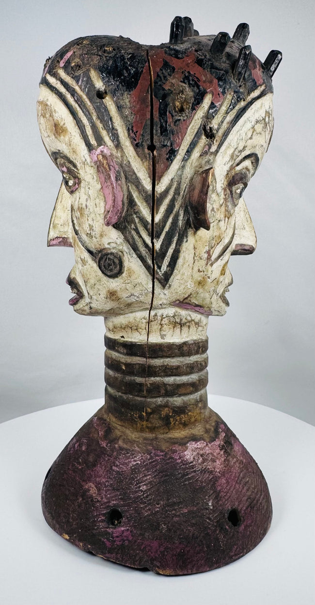 Mid-20th century Nigerian dance crest displaying two opposing human faces and traditional masquerade artistry.