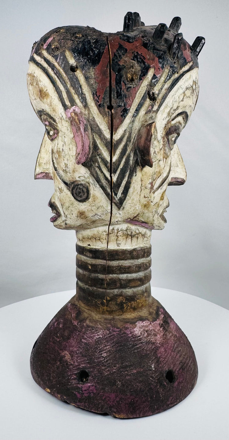 Mid-20th century Nigerian dance crest displaying two opposing human faces and traditional masquerade artistry.