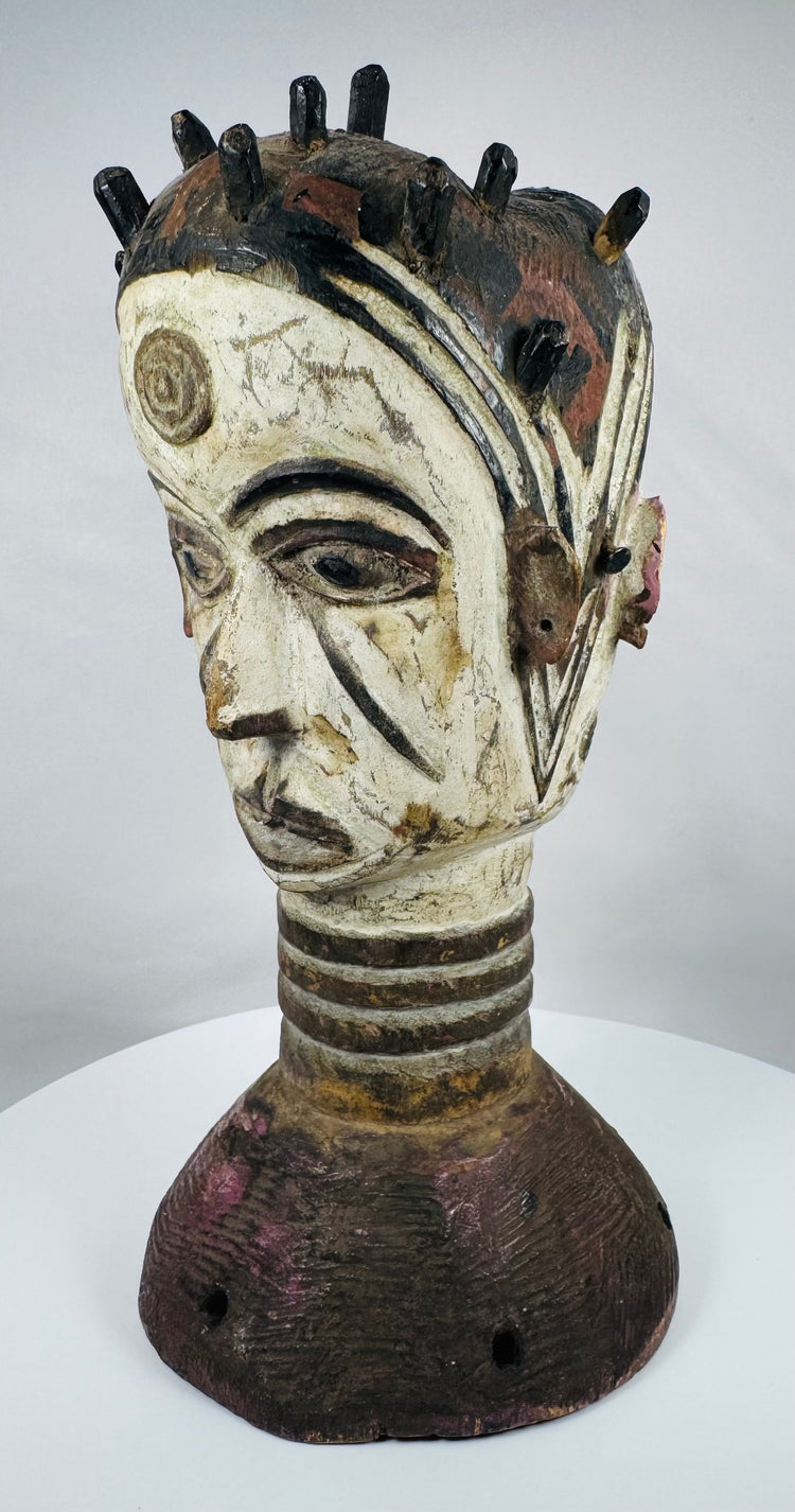Nigerian ceremonial headdress featuring a dual-faced carved design, ringed neck, and perforated base.