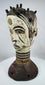 Nigerian ceremonial headdress featuring a dual-faced carved design, ringed neck, and perforated base.
