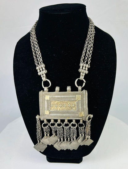 19th-century Omani silver hirz necklace with central rectangular Koran holder, intricate filigree and gilded accents, suspended from a multi-strand chain with decorative dangles.