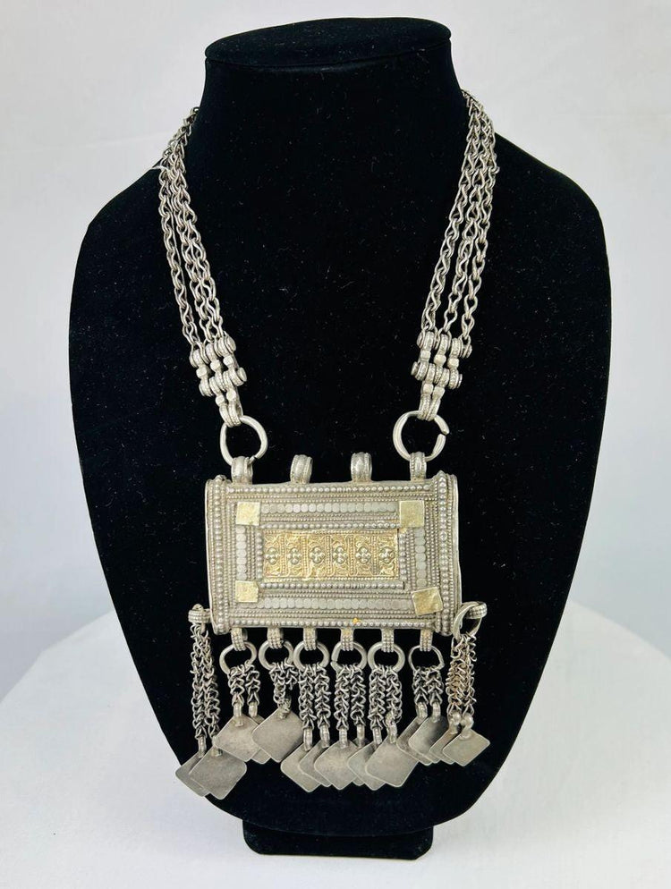 19th-century Omani silver hirz necklace with central rectangular Koran holder, intricate filigree and gilded accents, suspended from a multi-strand chain with decorative dangles.