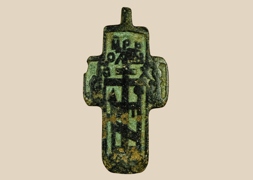 Small Russian Orthodox devotional cross-plaquette from the Old Believer tradition, cast in copper-alloy with champlevé green enamel remnants, blocky Cyrillic inscription panels, and deep olive patina, circa 1780–1820.