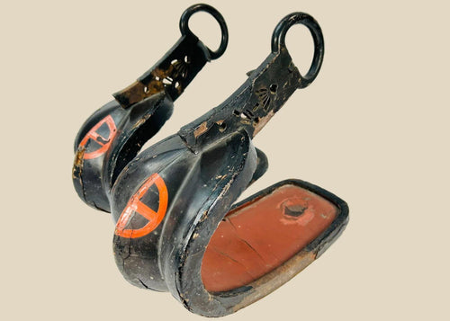 Matched pair of Edo–Meiji Japanese abumi (samurai stirrups) with black lacquer exterior, red interior, and Shimazu (Satsuma) clan cross-in-circle crest, featuring forged iron hangers and deep curved footbeds, circa 1800–1880.