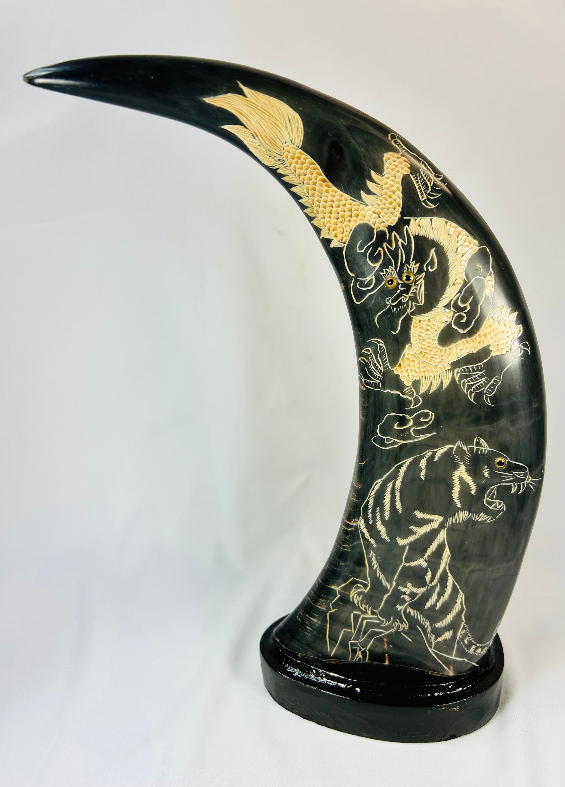 Mid–late 20th-century East Asian polished water buffalo horn sculptures etched and painted in gold with celestial dragons and prowling tigers amidst clouds, mounted on black lacquered bases, mirrored composition, circa 1960–1980.