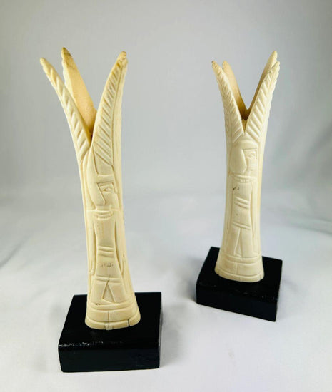 Pair of carved Egyptian ivory sistrum handles on black display bases, featuring stylized figures and decorative motifs, dating to the Third Intermediate Period, circa 1070–664 BCE.