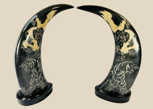 Mid–late 20th-century East Asian polished water buffalo horn sculptures etched and painted in gold with celestial dragons and prowling tigers amidst clouds, mounted on black lacquered bases, mirrored composition, circa 1960–1980.