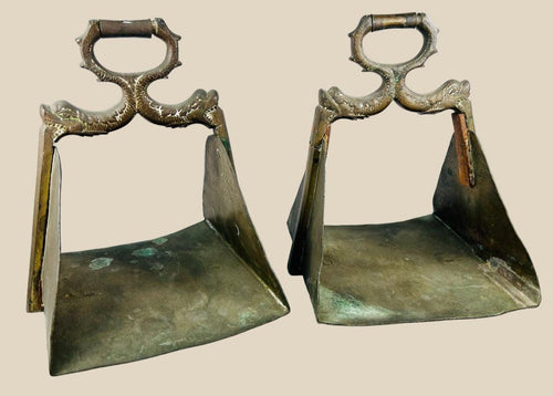 Antique pair of heavy brass equestrian stirrups with triangular footrests and intricately cast serpent motifs forming the handles, exhibiting detailed craftsmanship, natural patina, and symbolic protective design elements often associated with strength and guardianship in traditional horsemanship.