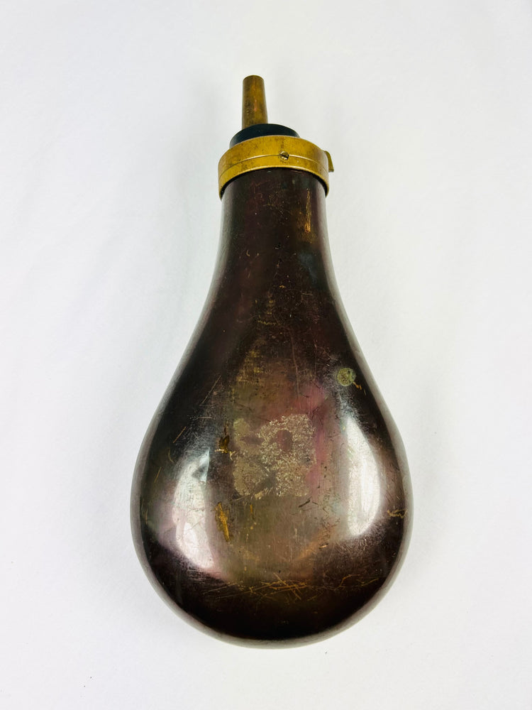 Antique 1840–1865 pressed copper powder flask with patriotic artillery and flag design, dark patina, brass collar and tapered spout, percussion firearm accessory.