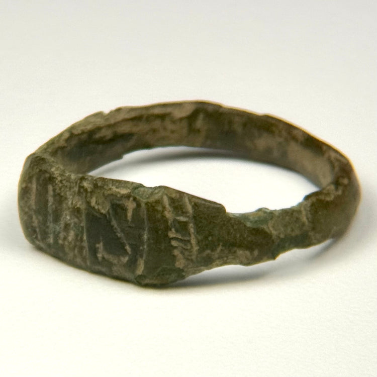 Close-up of ancient bronze ring bezel showing worn geometric engraving and dark green-brown patina
