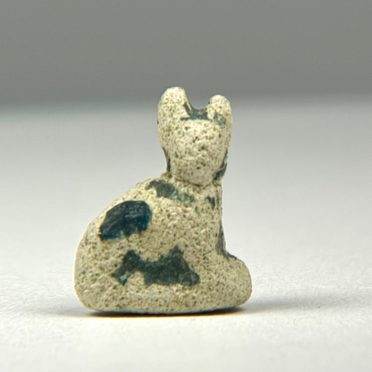 Small Ancient Egyptian Bastet cat amulet in faience with worn blue-green glaze and age-related surface encrustations.