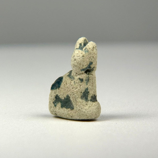 Ancient Egyptian seated cat amulet associated with the goddess Bastet, preserving remnants of its original turquoise-green glaze.