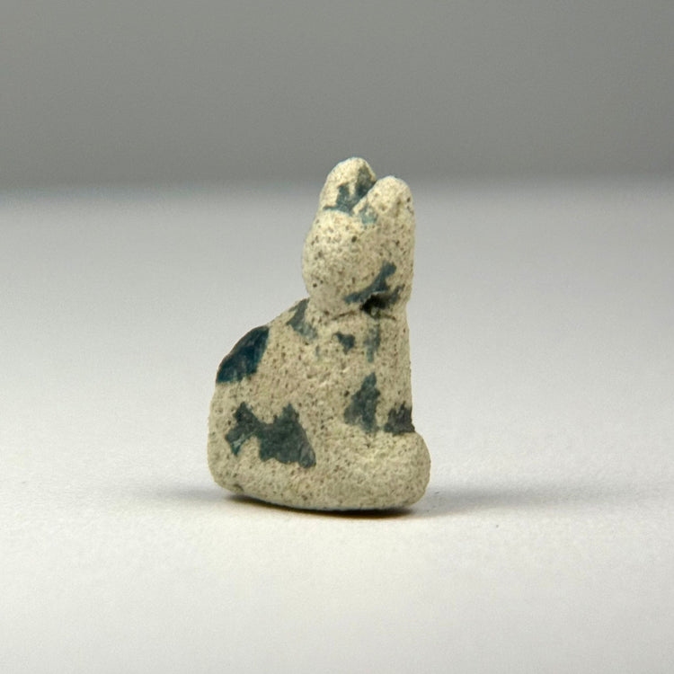 Ancient Egyptian seated cat amulet associated with the goddess Bastet, preserving remnants of its original turquoise-green glaze.