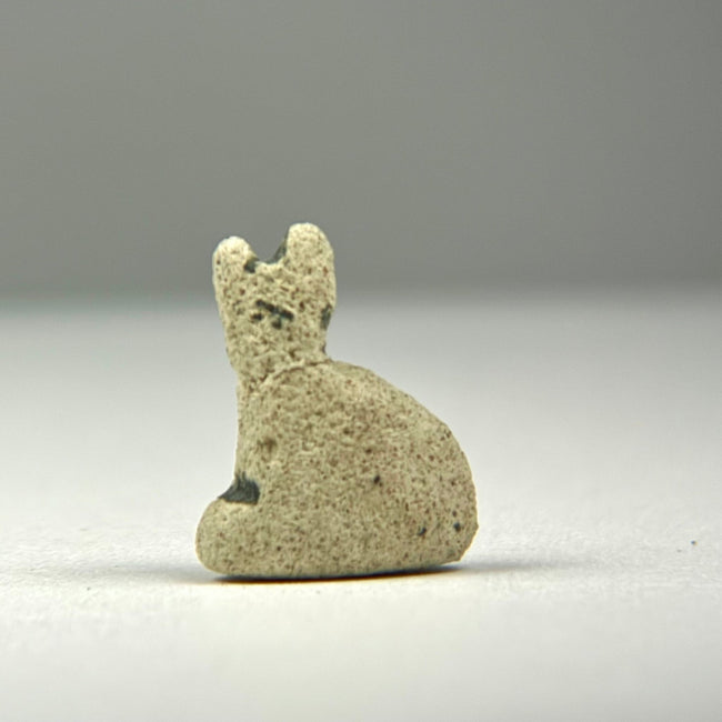 Small faience Bastet amulet from Ancient Egypt with textured earthen deposits and surviving areas of blue-green glazing.