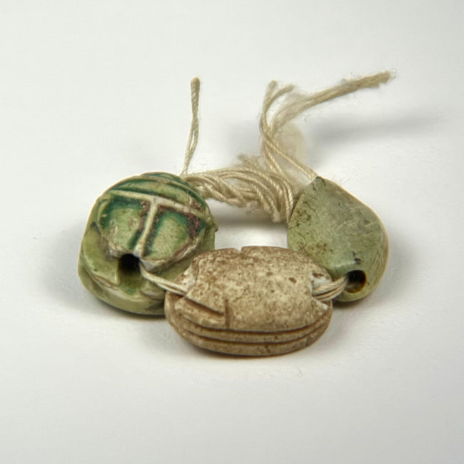 Three Ancient Egyptian scarab charms with varied surface preservation, carved details, hieroglyphic markings, and traces of green glaze.