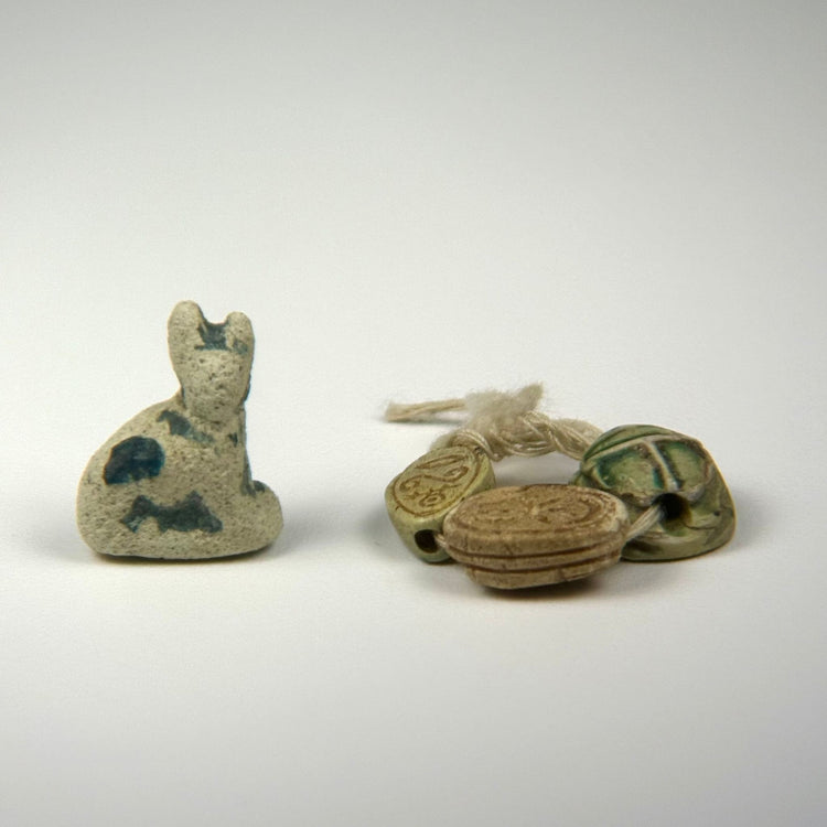 Ancient Egyptian faience Bastet cat amulet displayed with three scarab charms, dating from the Late Period to Ptolemaic Period.