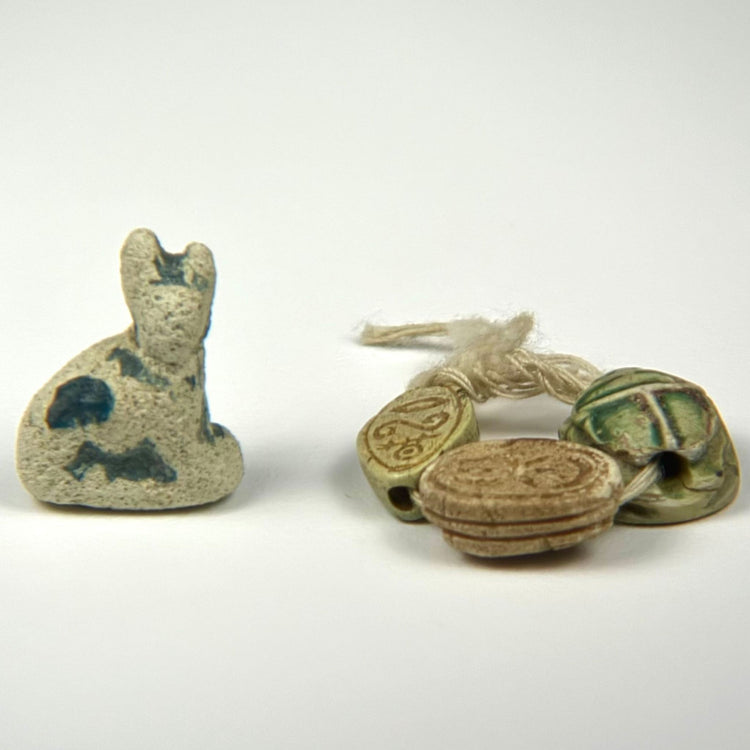 Collection of Ancient Egyptian amulets featuring a seated faience cat and three carved scarabs with surviving glaze and incised decoration.