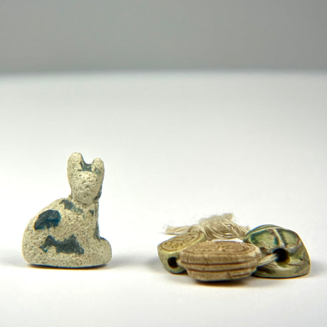Group of Ancient Egyptian protective charms including a blue-green faience cat amulet and three individually carved scarabs.