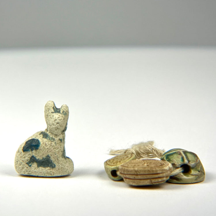 Group of Ancient Egyptian protective charms including a blue-green faience cat amulet and three individually carved scarabs.