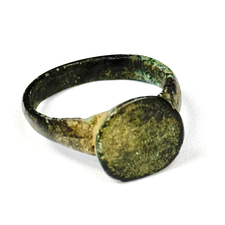 Close view of ancient bronze ring showing broad flat bezel, irregular handmade profile, and mineralized surface deposits