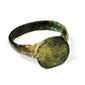 Close view of ancient bronze ring showing broad flat bezel, irregular handmade profile, and mineralized surface deposits