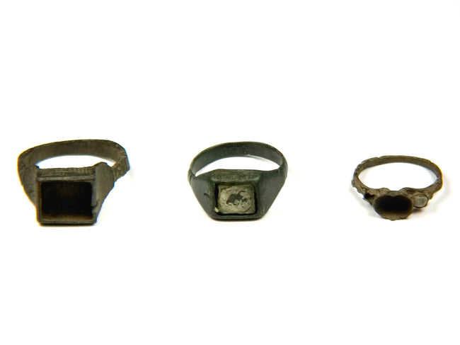 Three Late Roman to Early Byzantine bronze finger rings displayed side by side, featuring square bezel, inset signet and round bezel designs, circa 3rd–7th century CE