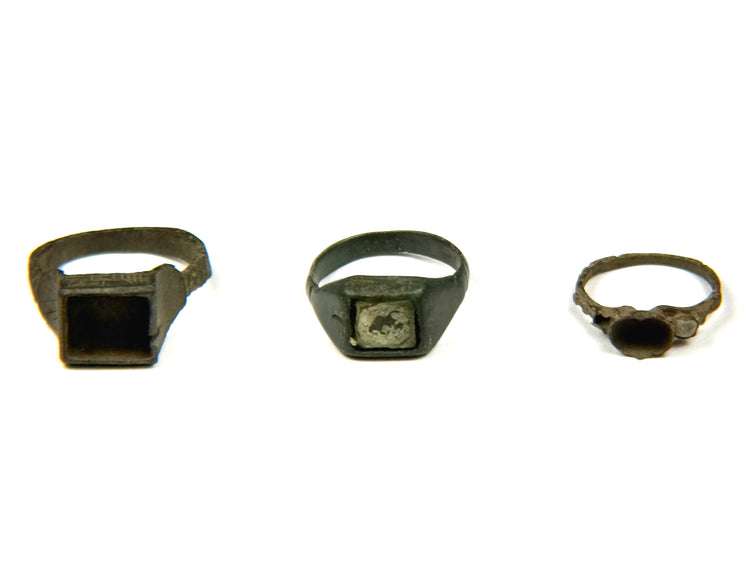 Three Late Roman to Early Byzantine bronze finger rings displayed side by side, featuring square bezel, inset signet and round bezel designs, circa 3rd–7th century CE