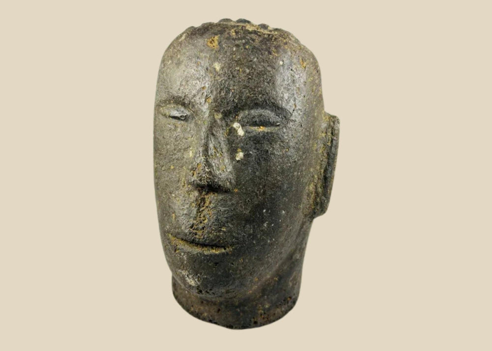 Antique Polynesian volcanic stone head sculpture, carved with stylized facial features and linear hair details, used for ancestor veneration, photographed on a white background.